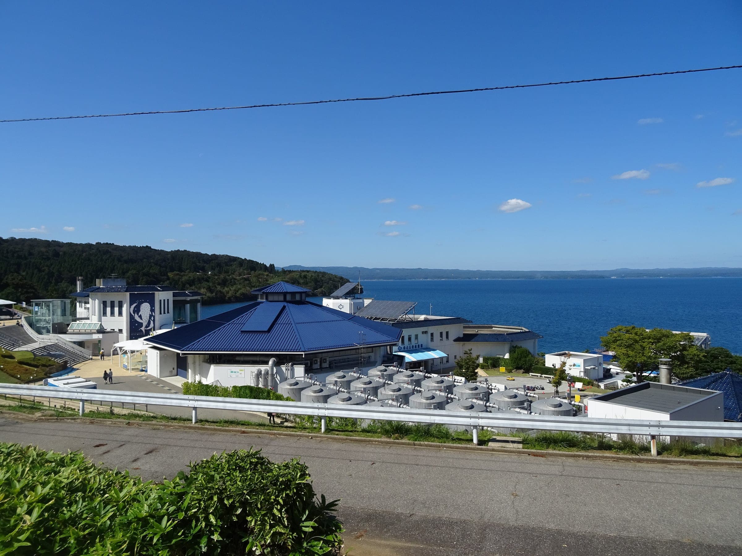 Notojima Aquarium's blue-roofed buildings sit on a hillside above the calm water of Nanao Bay
