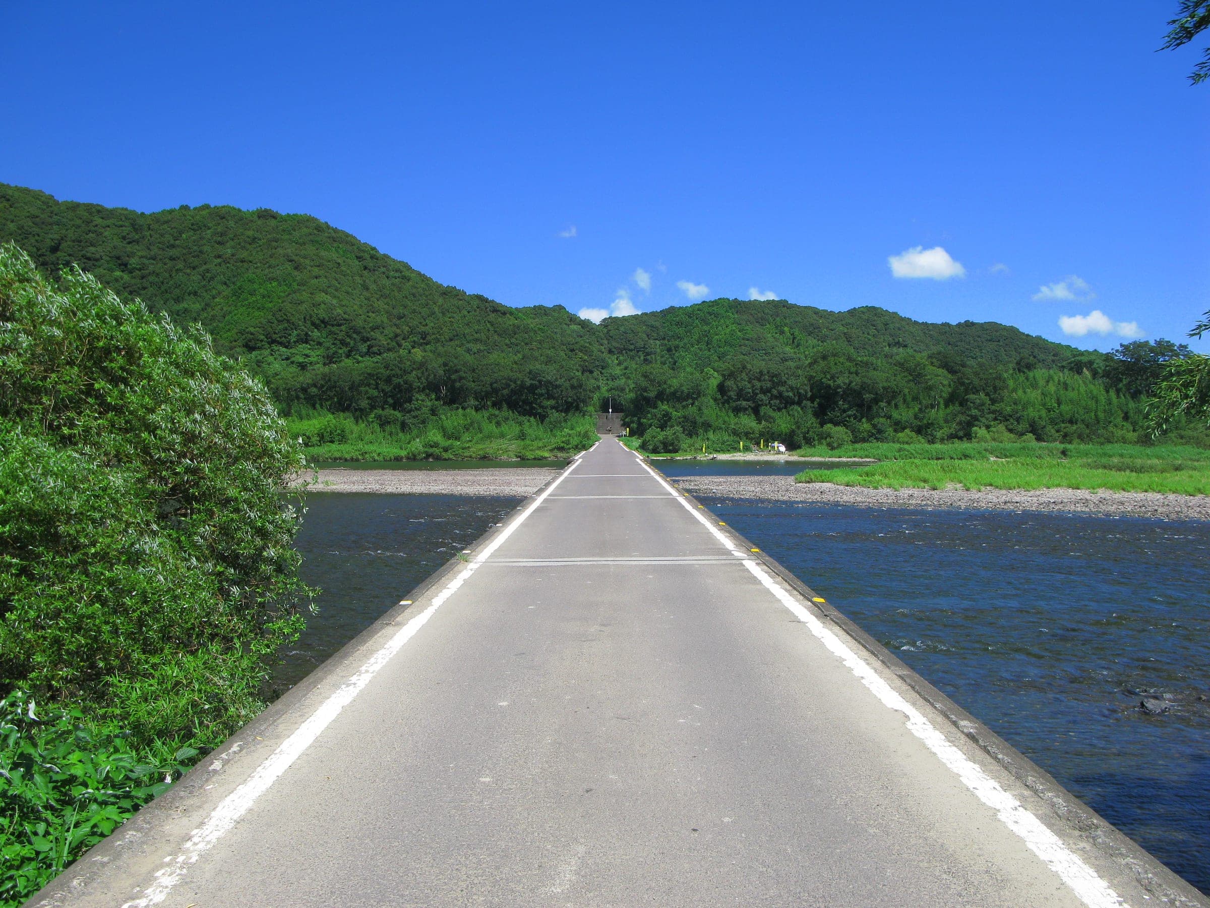 The railing-free deck of the Sada sinking bridge runs straight across the Shimanto River in summer.