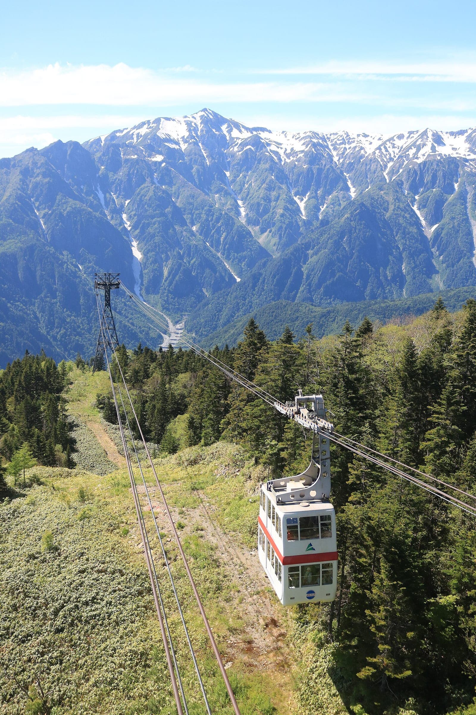 A double-decker gondola of the Shin-Hotaka Ropeway climbs over forest toward the Hotaka range in June