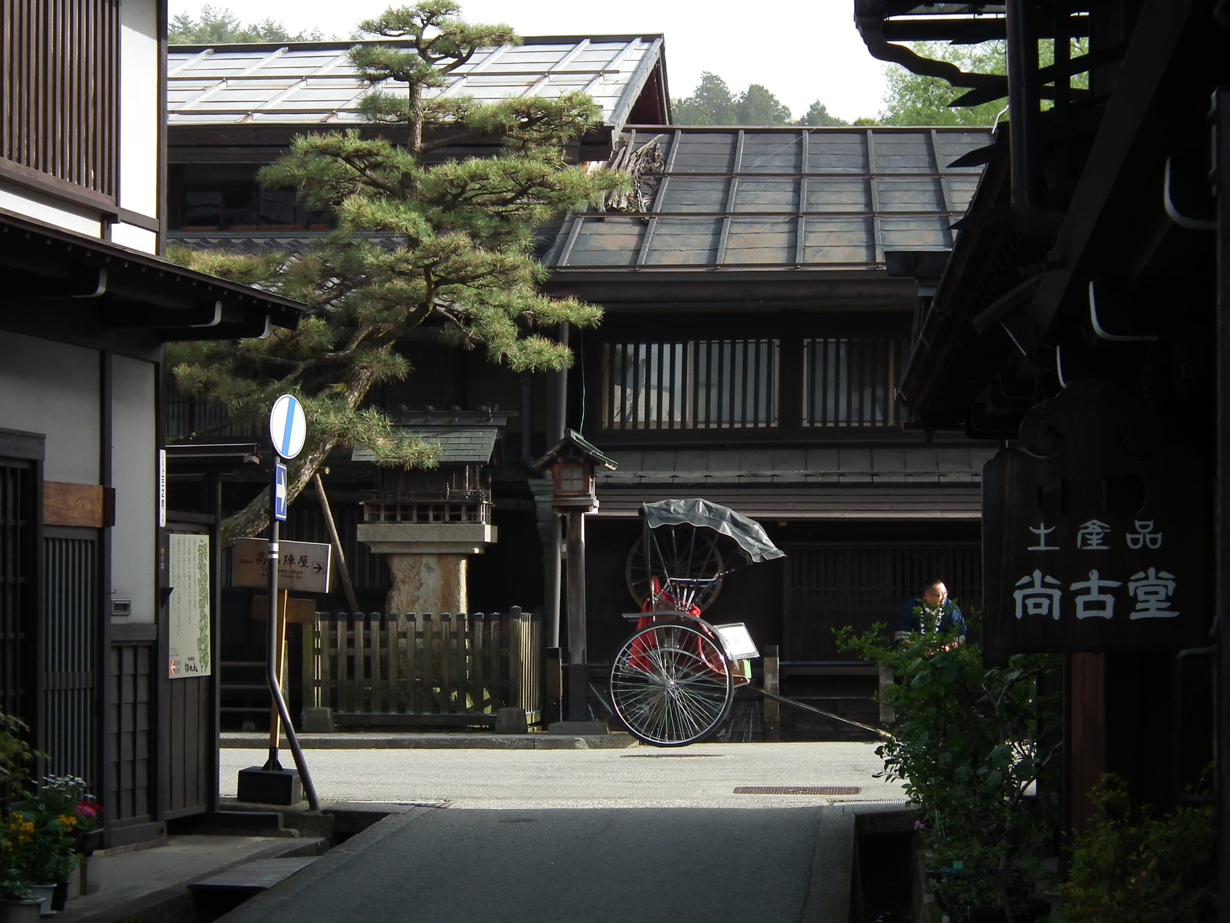 A rickshaw waits under a pine outside wooden shopfronts in the Sanmachi district of Takayama