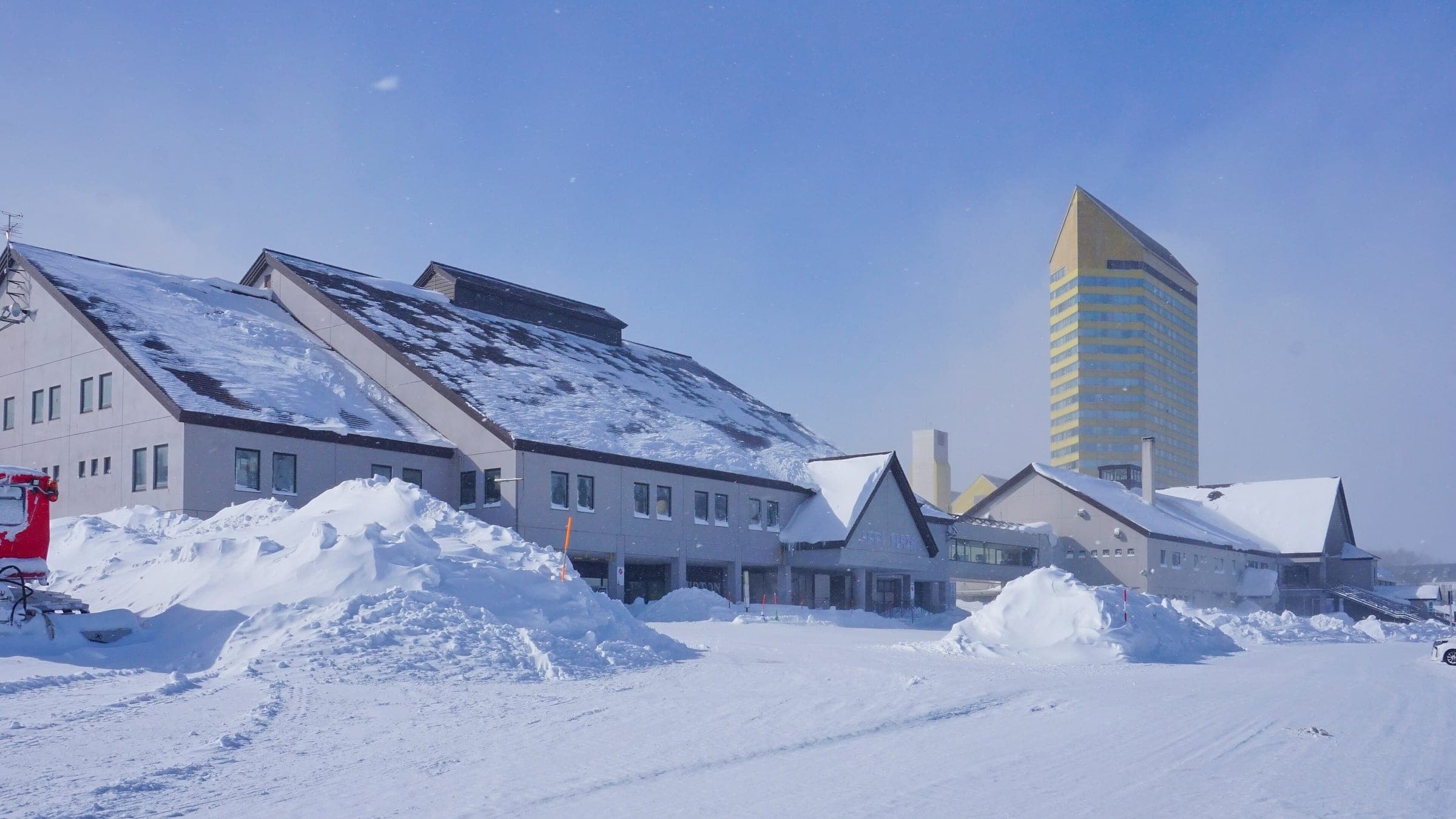 The yellow tower of the ANA Crowne Plaza Resort Appi Kogen rises behind snowed-in base lodges at APPI.