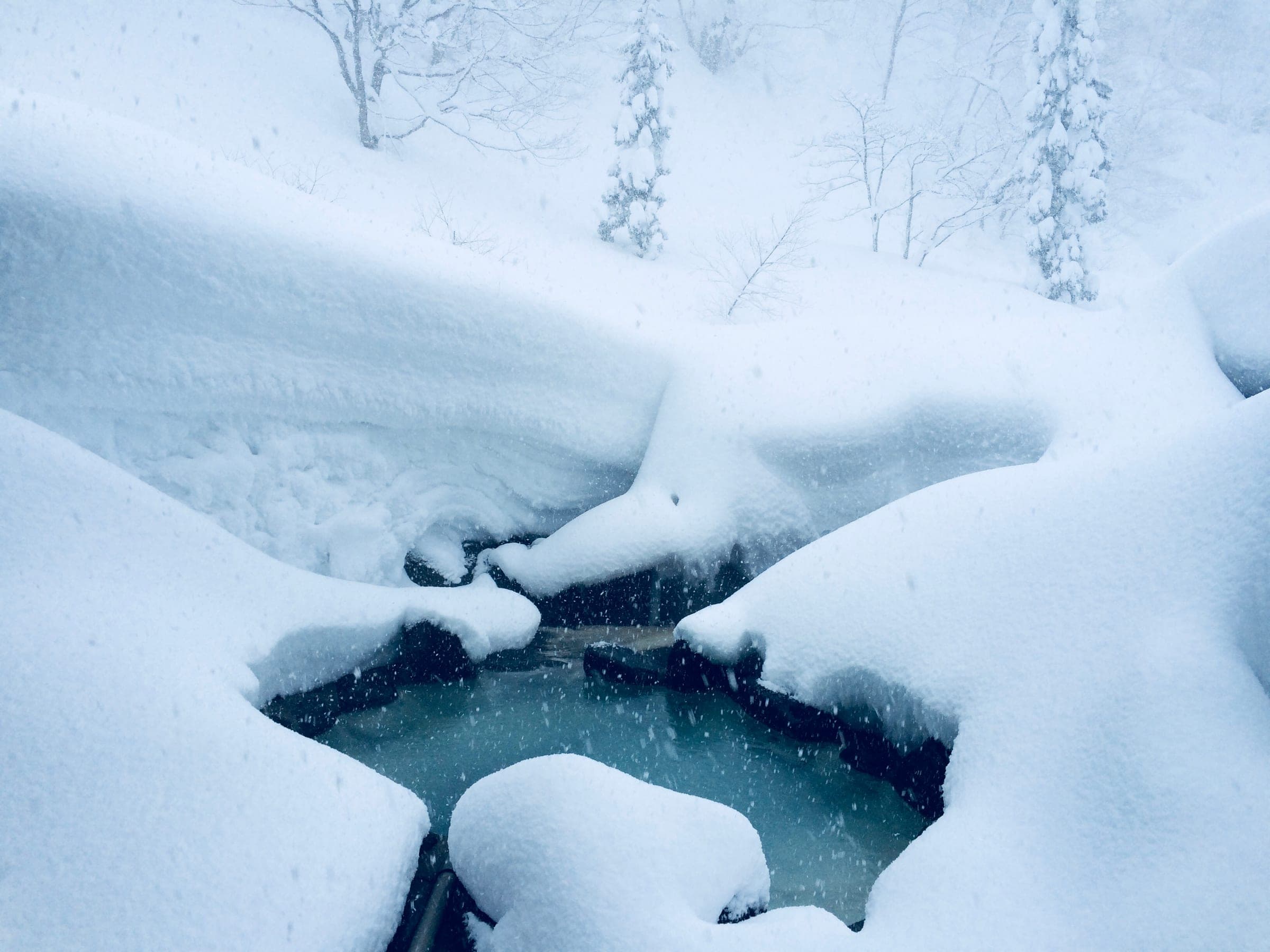 Fresh snow banks up around the blue-green outdoor bath at Magoroku Onsen in February.