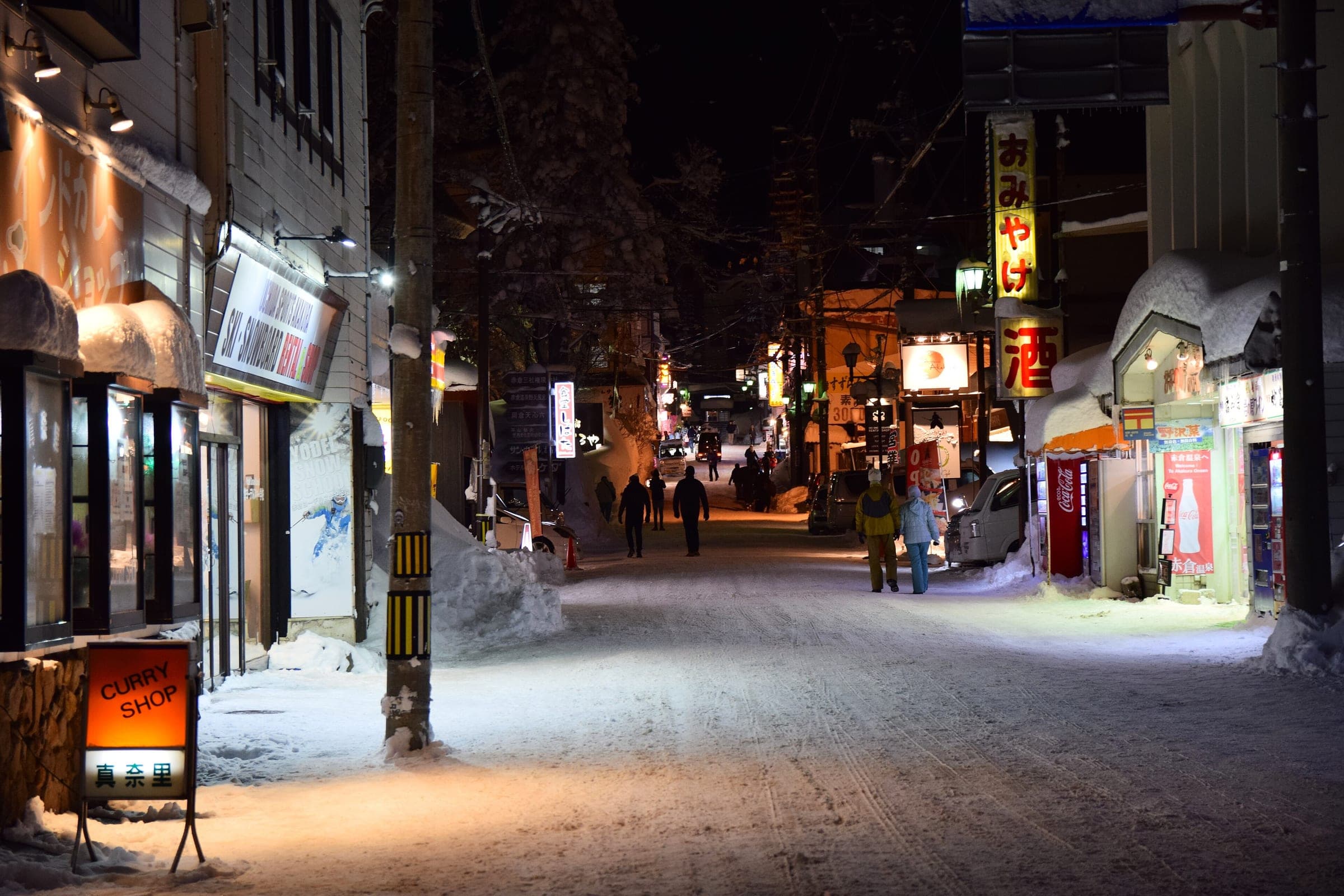 Shop lights glow along the snowy main street of Akakura Onsen on a winter night