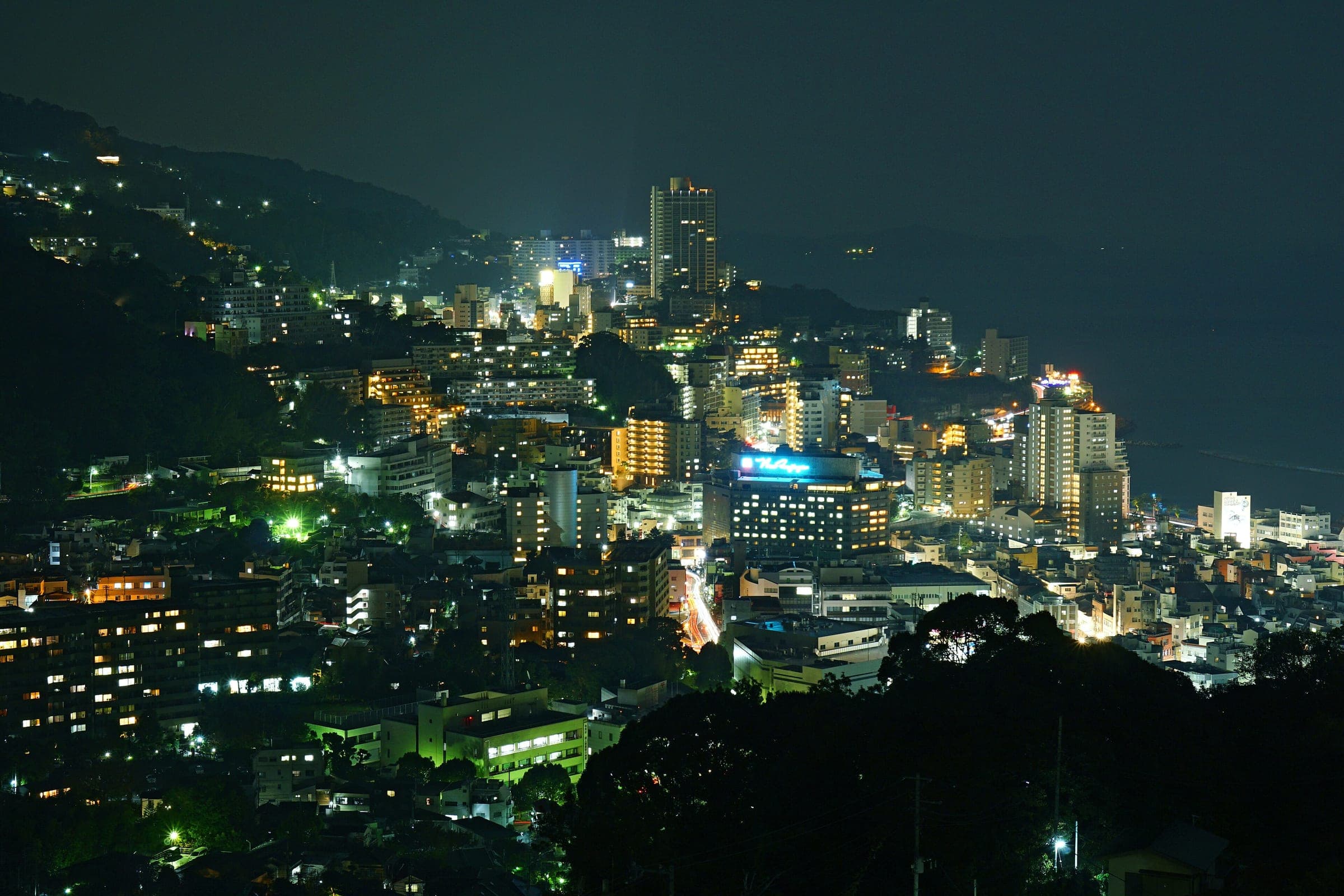 Hotel lights fill the slopes of Atami Onsen at night above the curve of the bay.