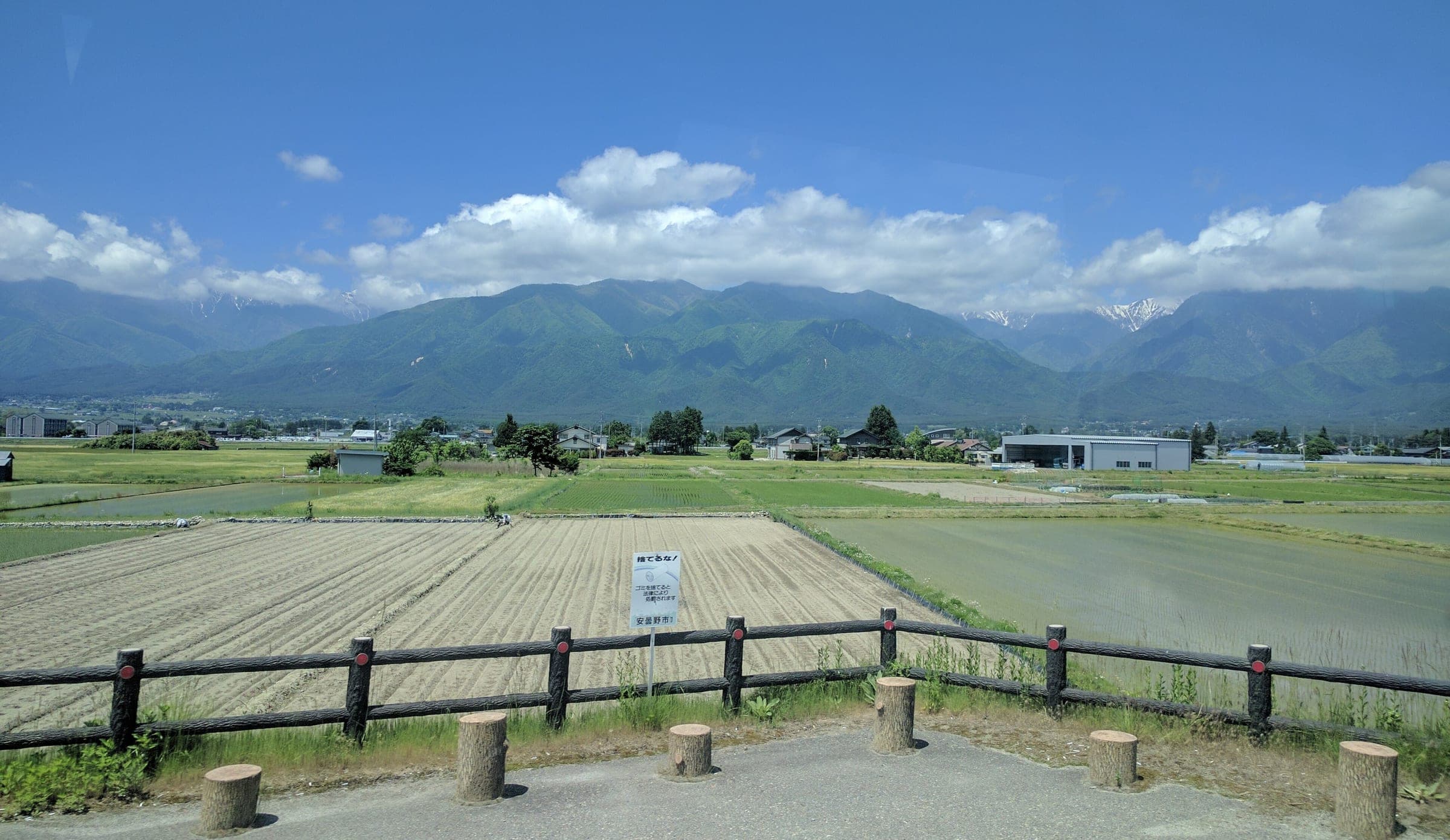 Tilled fields spread across the Azumino plain under the green foothills of the Northern Alps in May.
