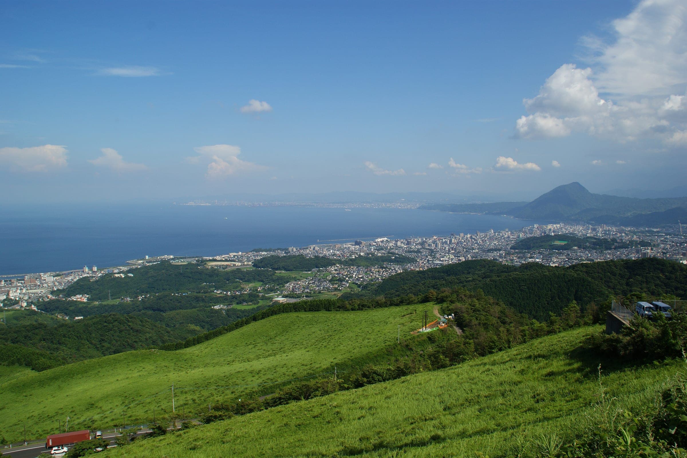 Green slopes at Jumonjibaru fall to the city of Beppu and the wide blue curve of Beppu Bay.