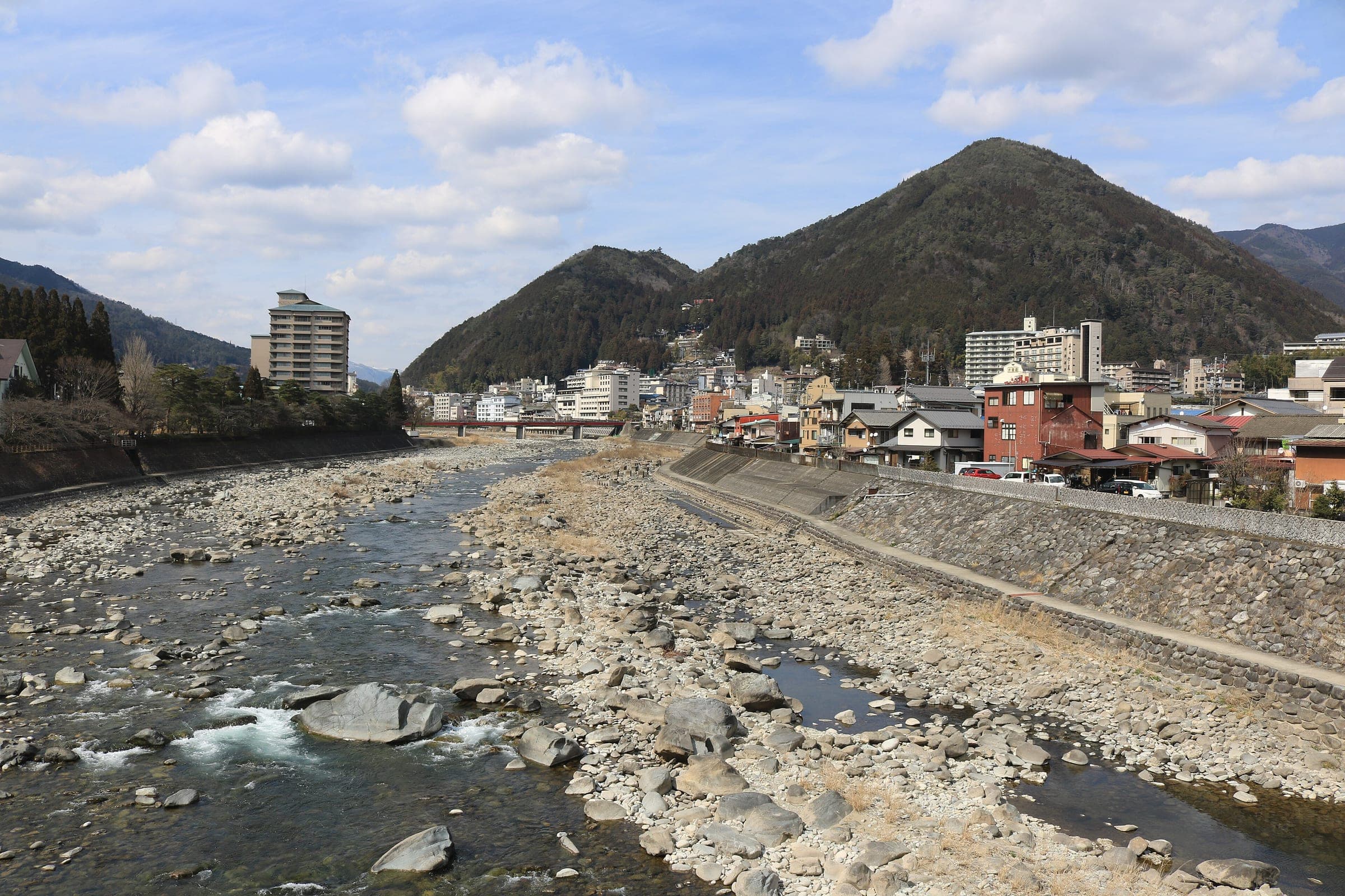 The rocky Hida River leads to the hotels and wooded hills of Gero Onsen in the view from Mutsumi Bridge