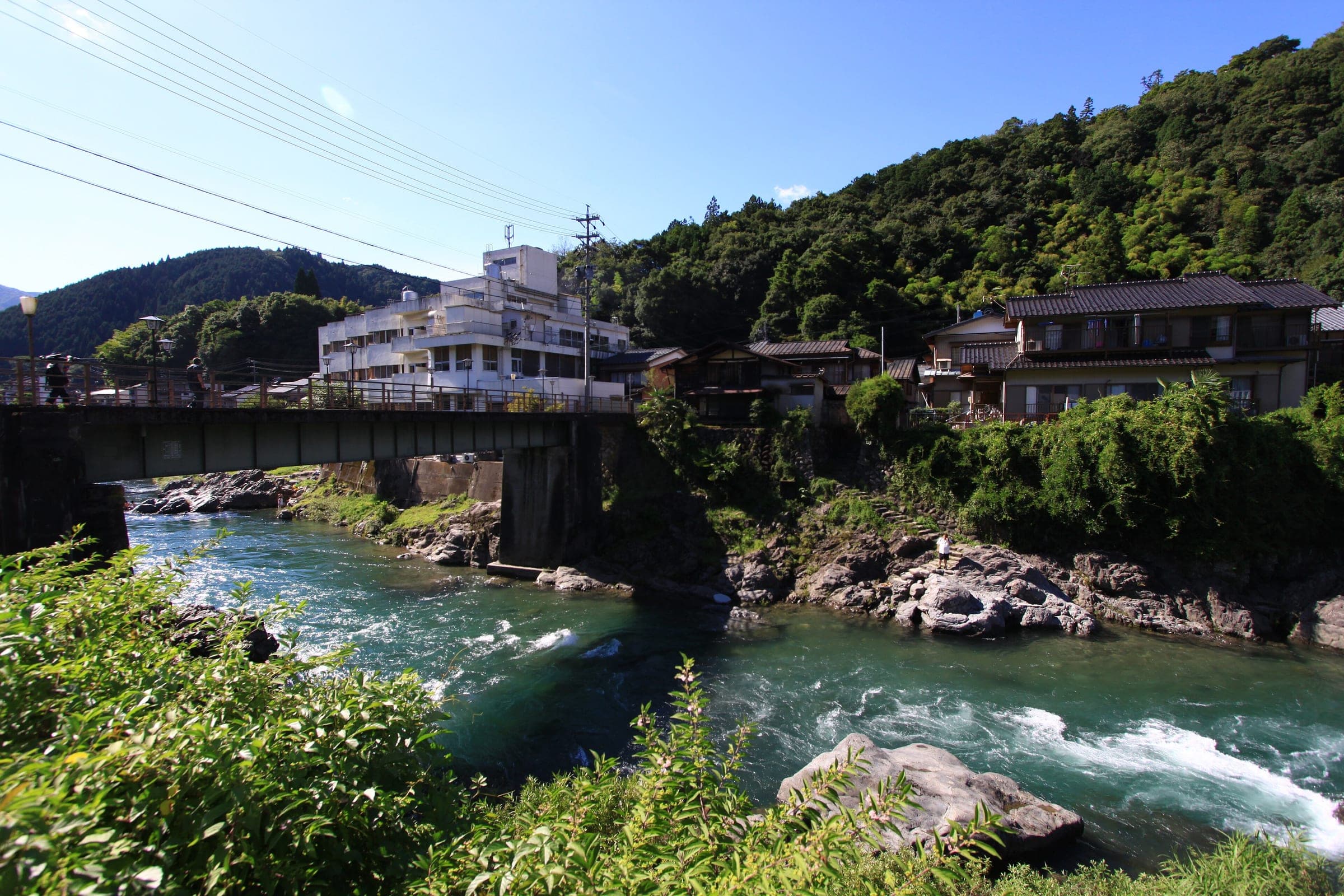 The clear Yoshida River rushes over rocks below houses and a bridge in Gujo-Hachiman