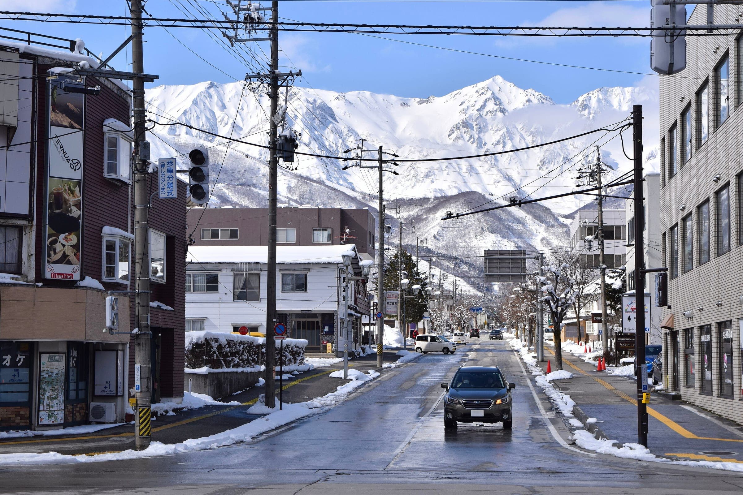 A snowy street in Hakuba village leads toward the white Hakuba Sanzan peaks in February.
