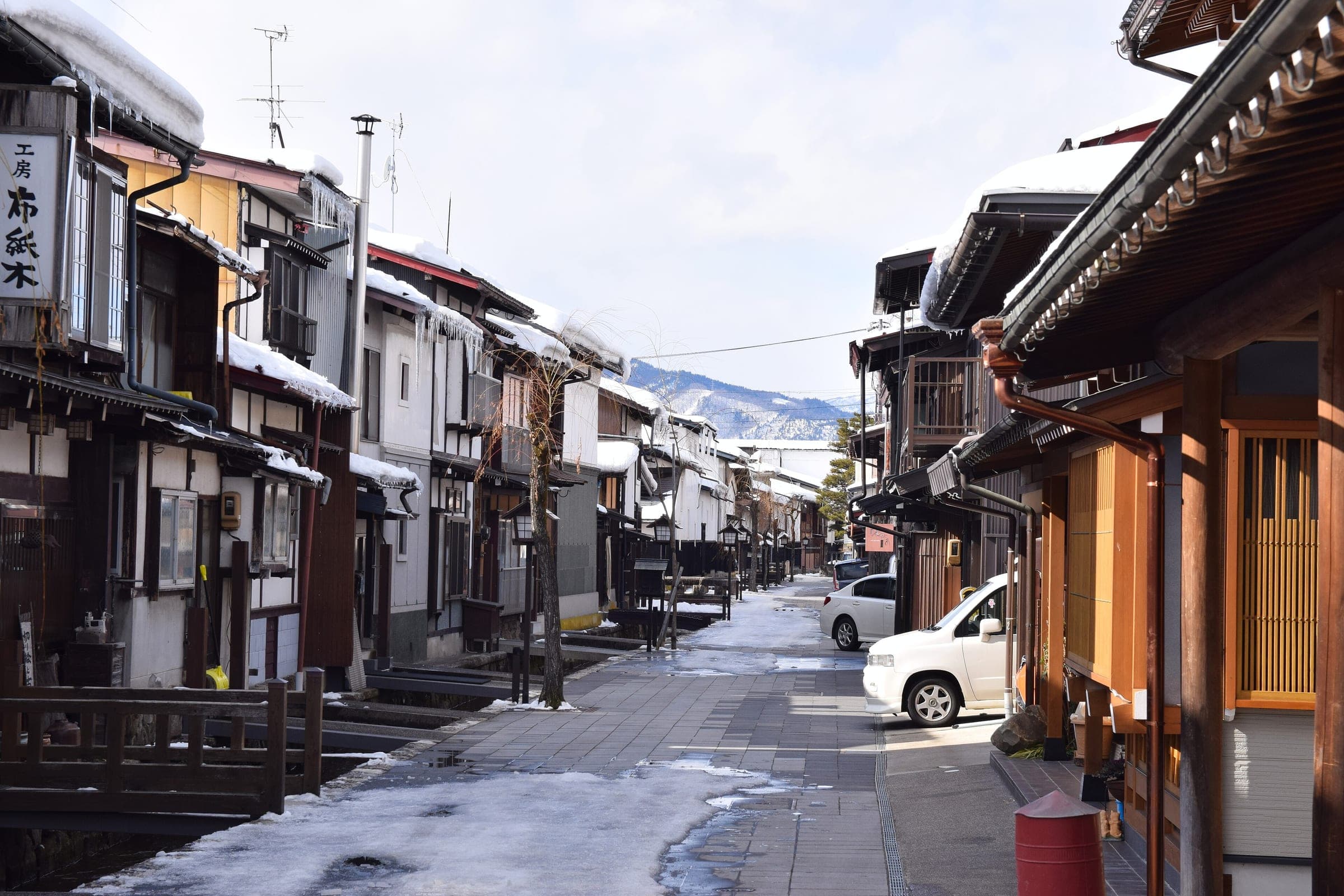 Wooden townhouses with snow on their eaves line a quiet street in Hida-Furukawa