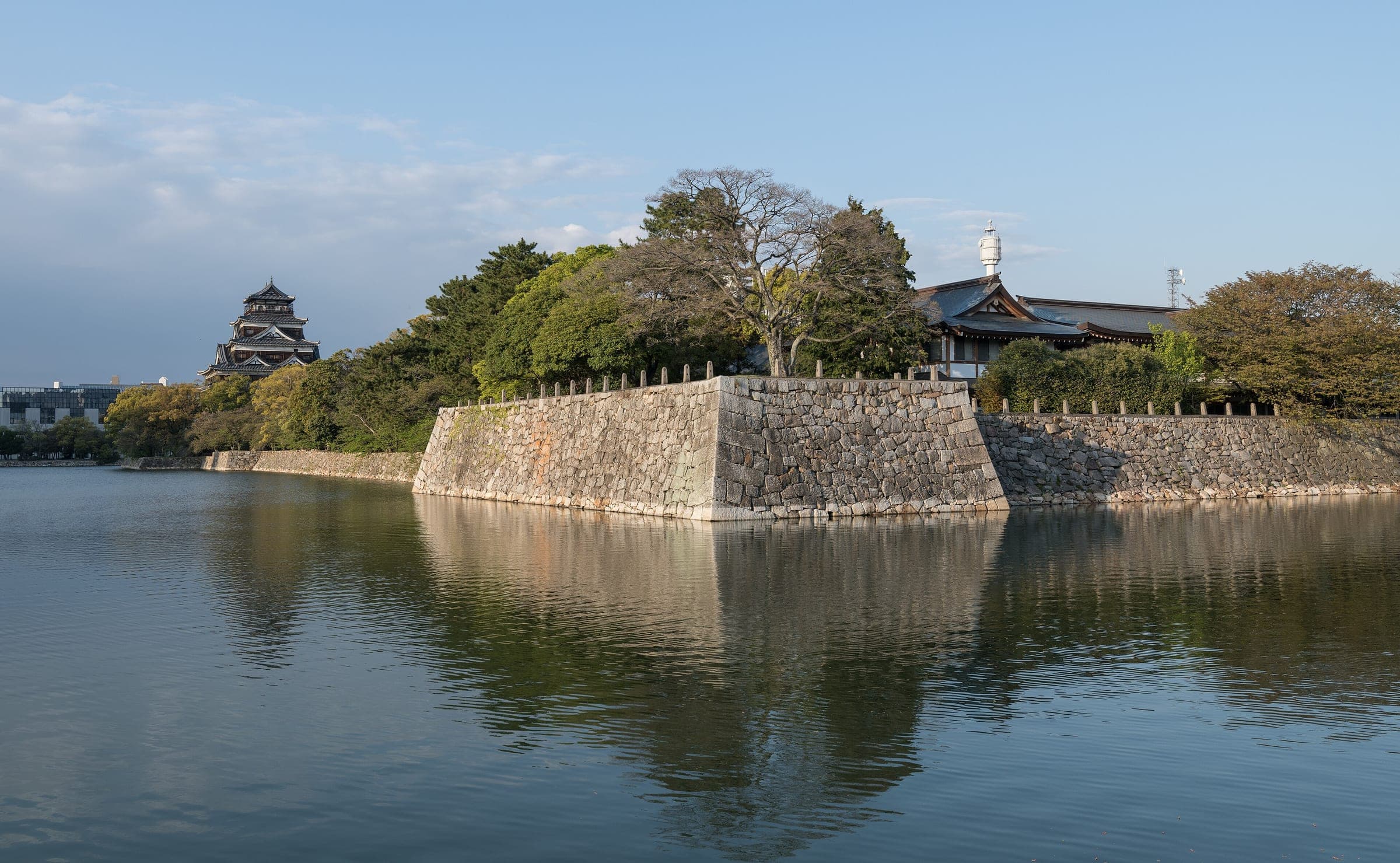 Hiroshima Castle's keep and stone walls reflect in the still west moat in soft evening light.