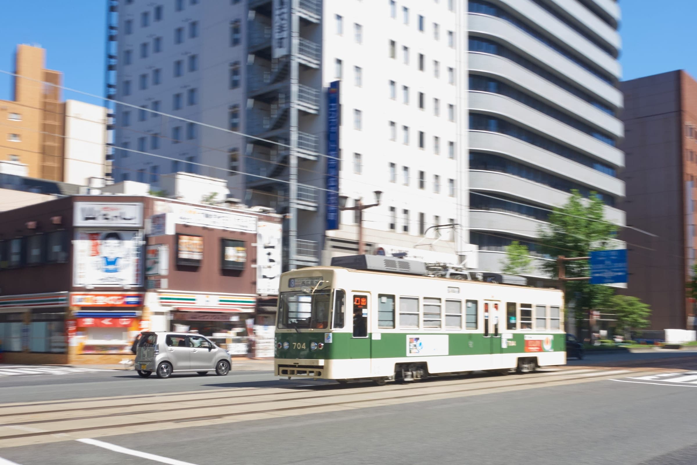 A green-and-cream Hiroden tram runs past offices along a wide street in central Hiroshima.