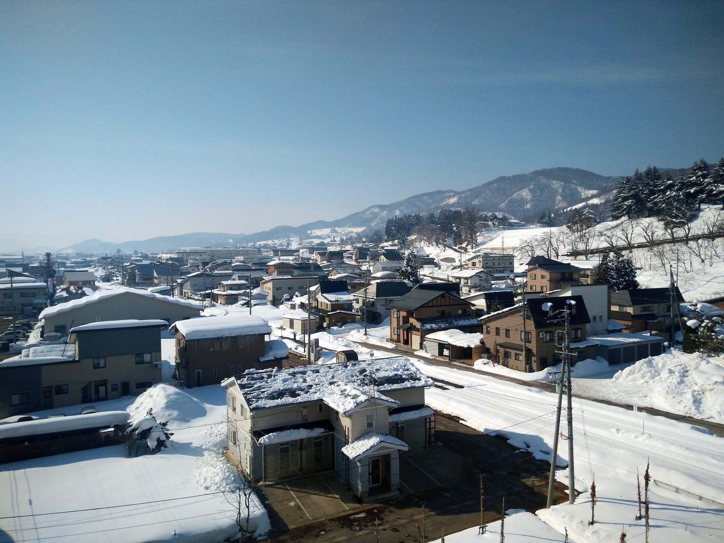 Deep February snow lies on the rooftops and lanes of Iiyama below its wooded hills.