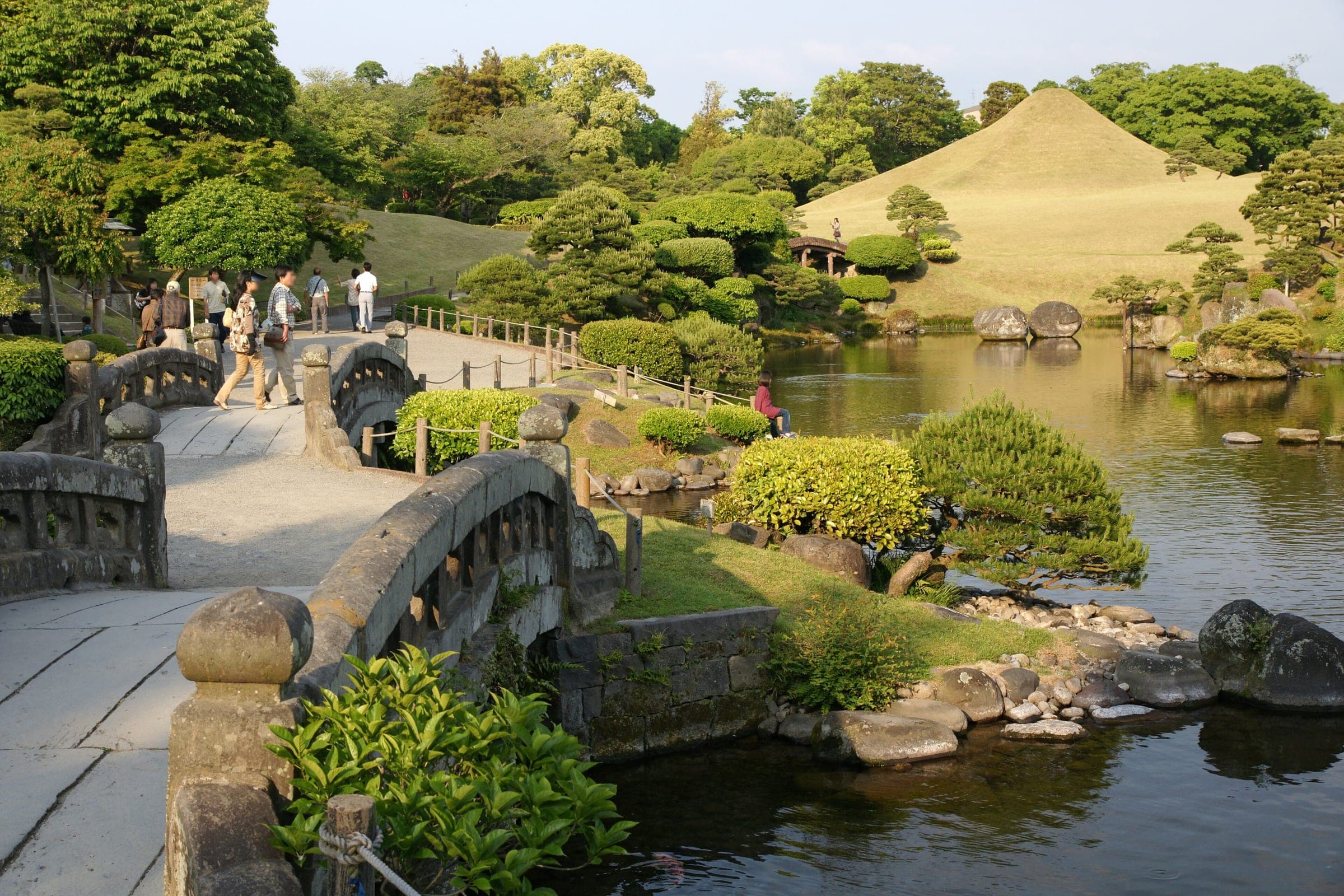 Late sun lights the stone bridges, spring-fed pond and grassy mini-Fuji of Suizenji Jojuen garden in Kumamoto.