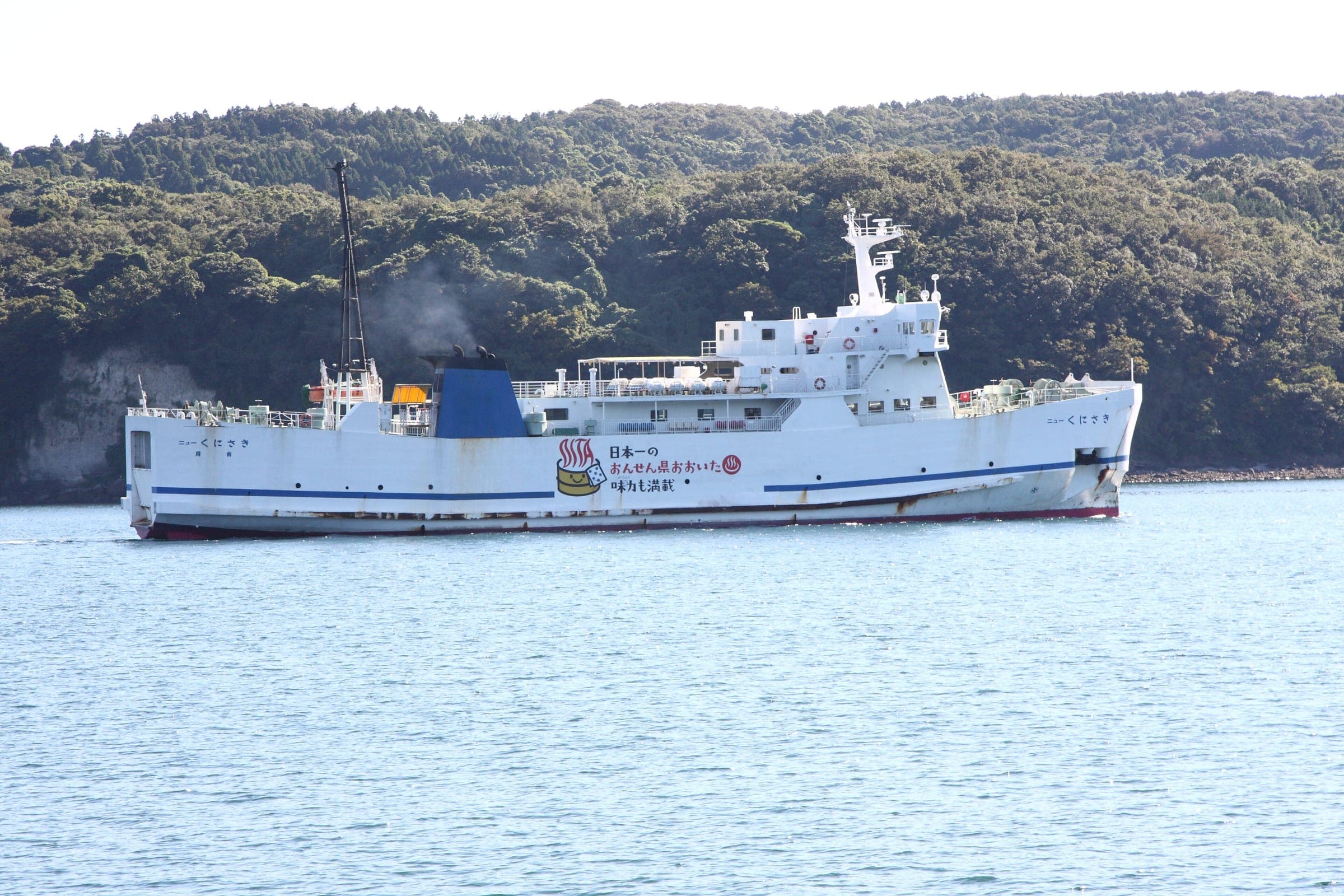 The ferry New Kunisaki sails into Taketazu port past the wooded shore of Kunisaki.
