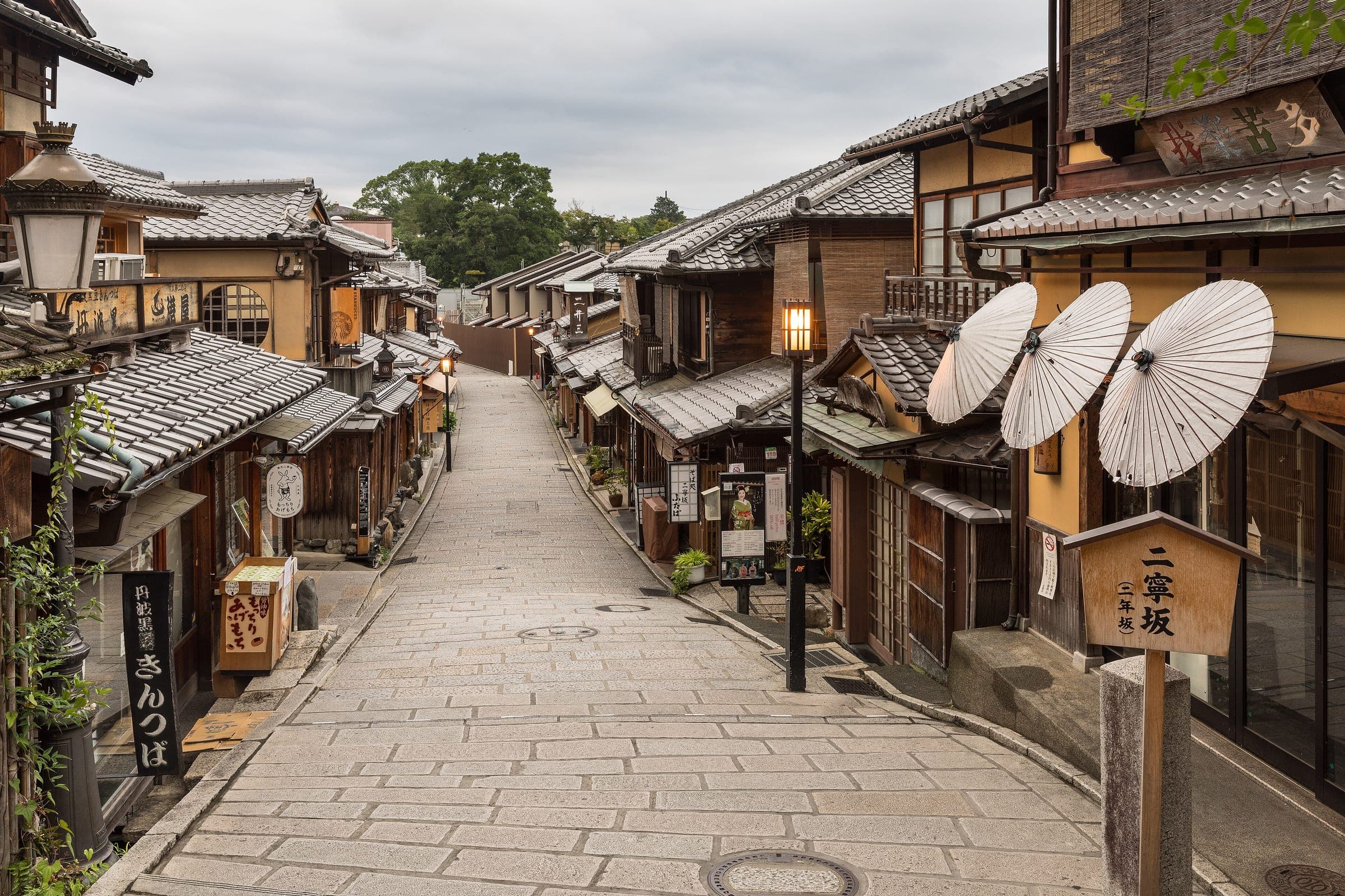 Paper umbrellas lean outside timber shopfronts on the stone lane of Ninenzaka in Kyoto