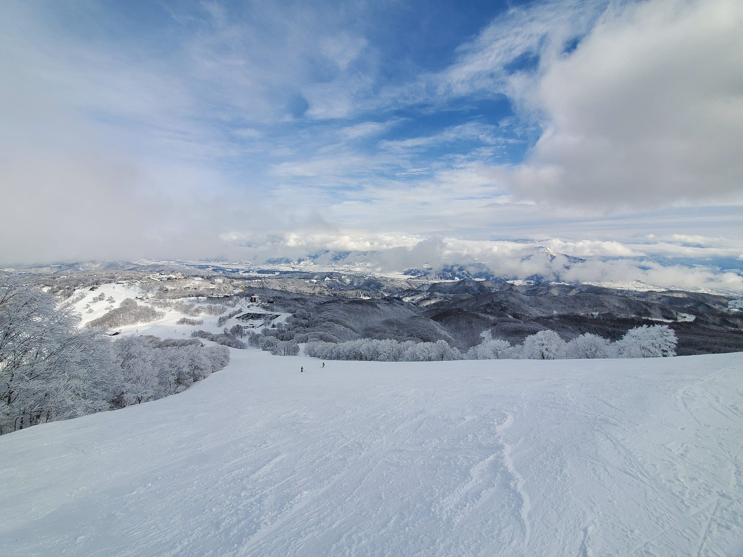 A wide groomed run at Madarao Kogen opens onto a view of snowy hills and low cloud in January.