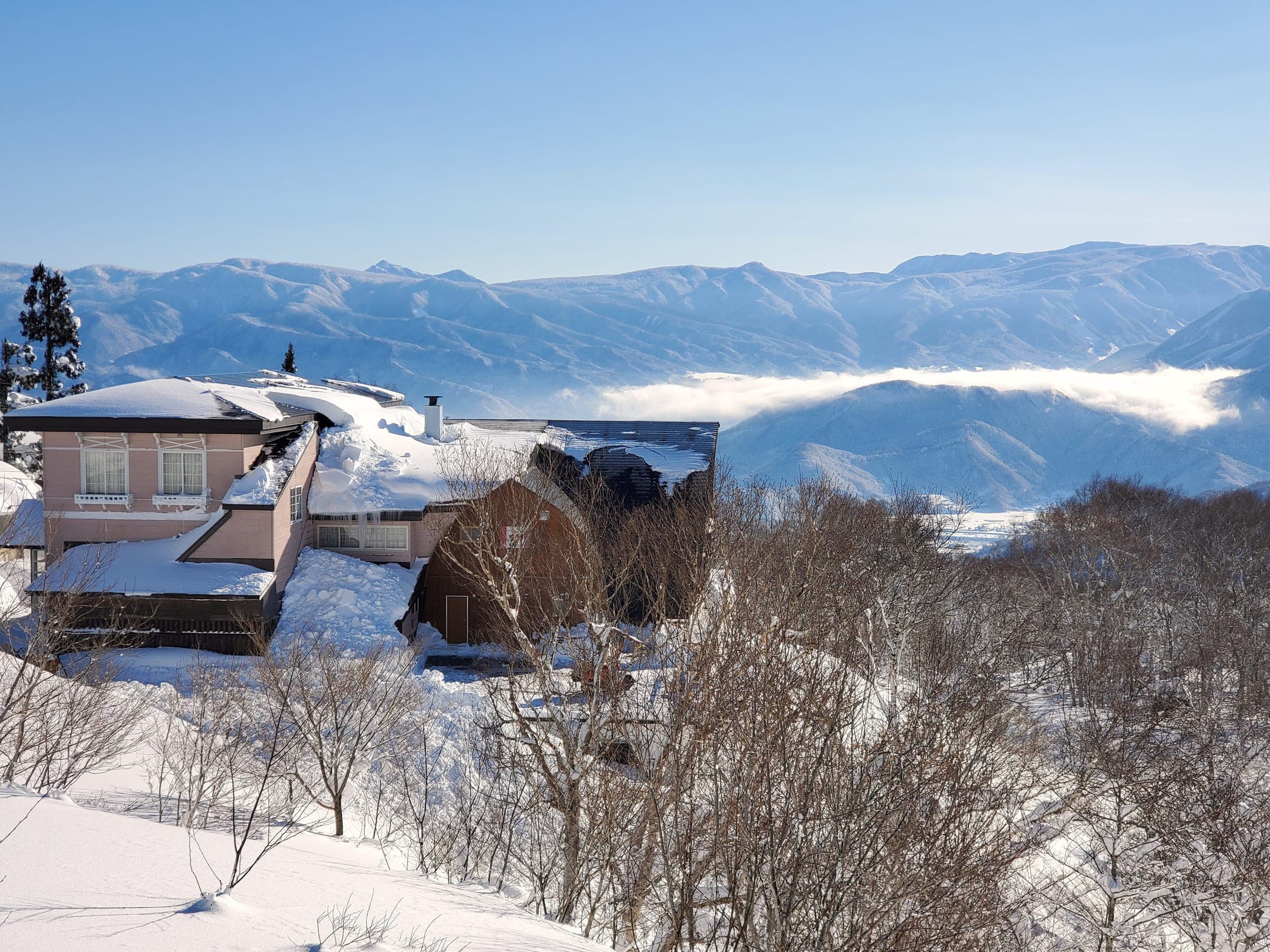 A snowy lodge at Madarao Kogen looks out over a sea of cloud and the mountains beyond on a January morning.