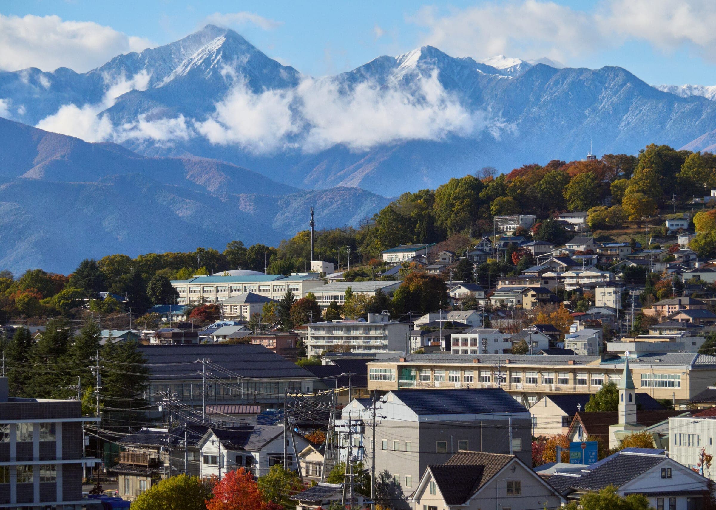 Snow-capped Northern Alps peaks rise behind the rooftops of Matsumoto in late autumn.