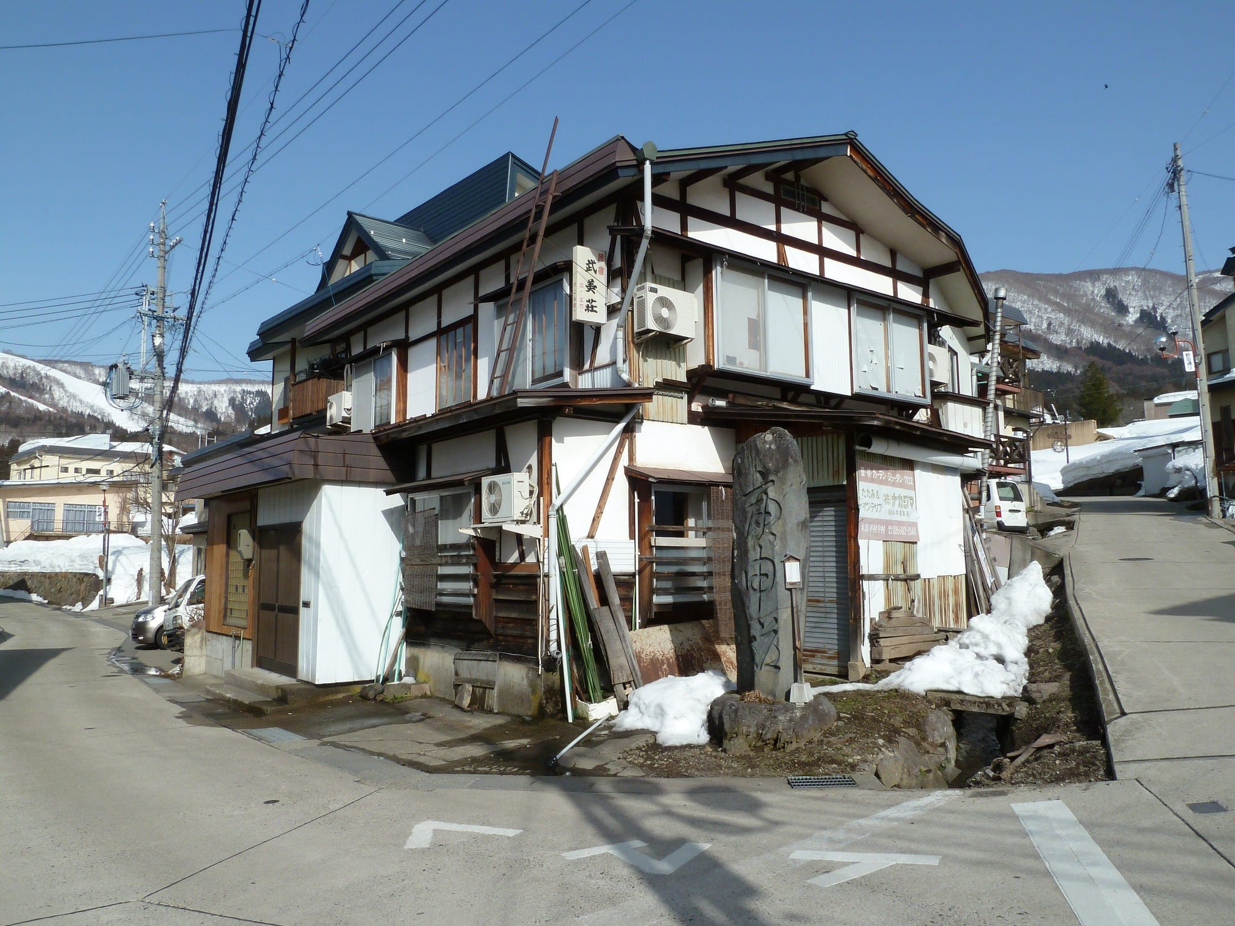 Old timber houses and banked snow line a street corner in Nozawa Onsen village.