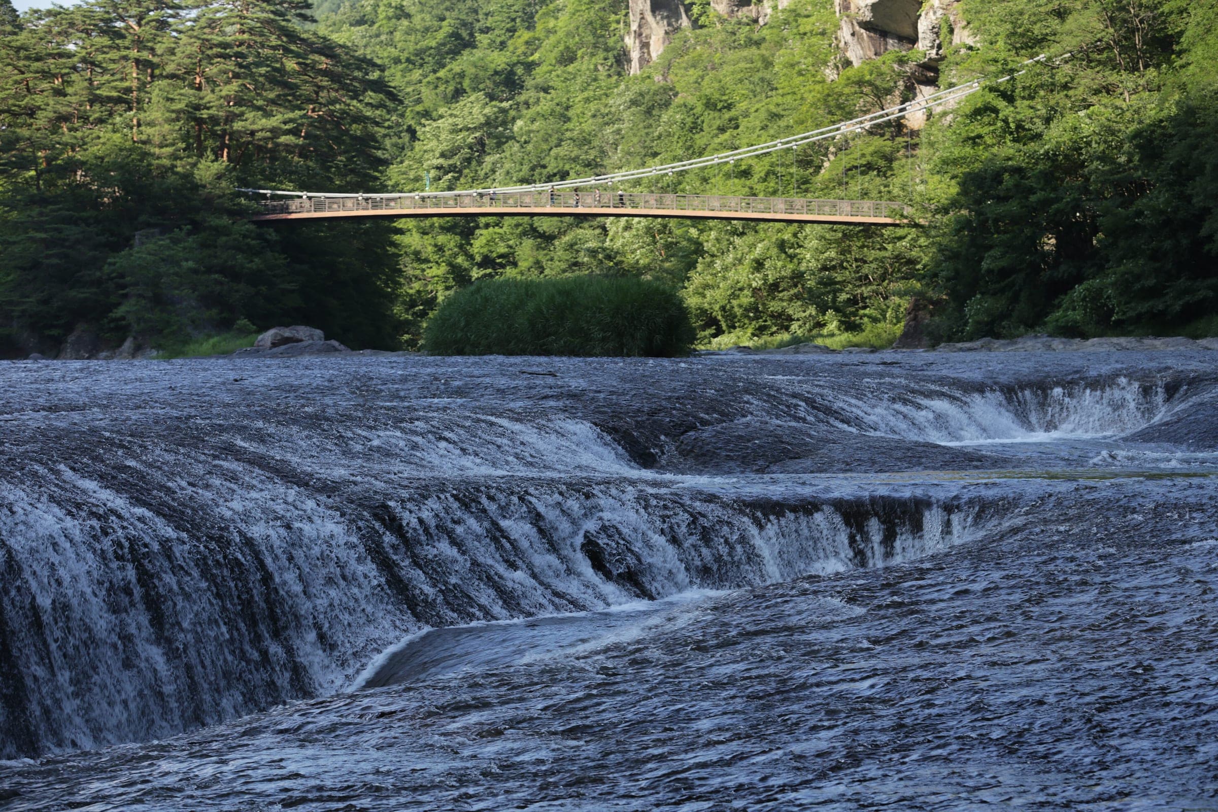 The Katashina River pours over the wide rock shelves of Fukiware Falls in Numata below a footbridge