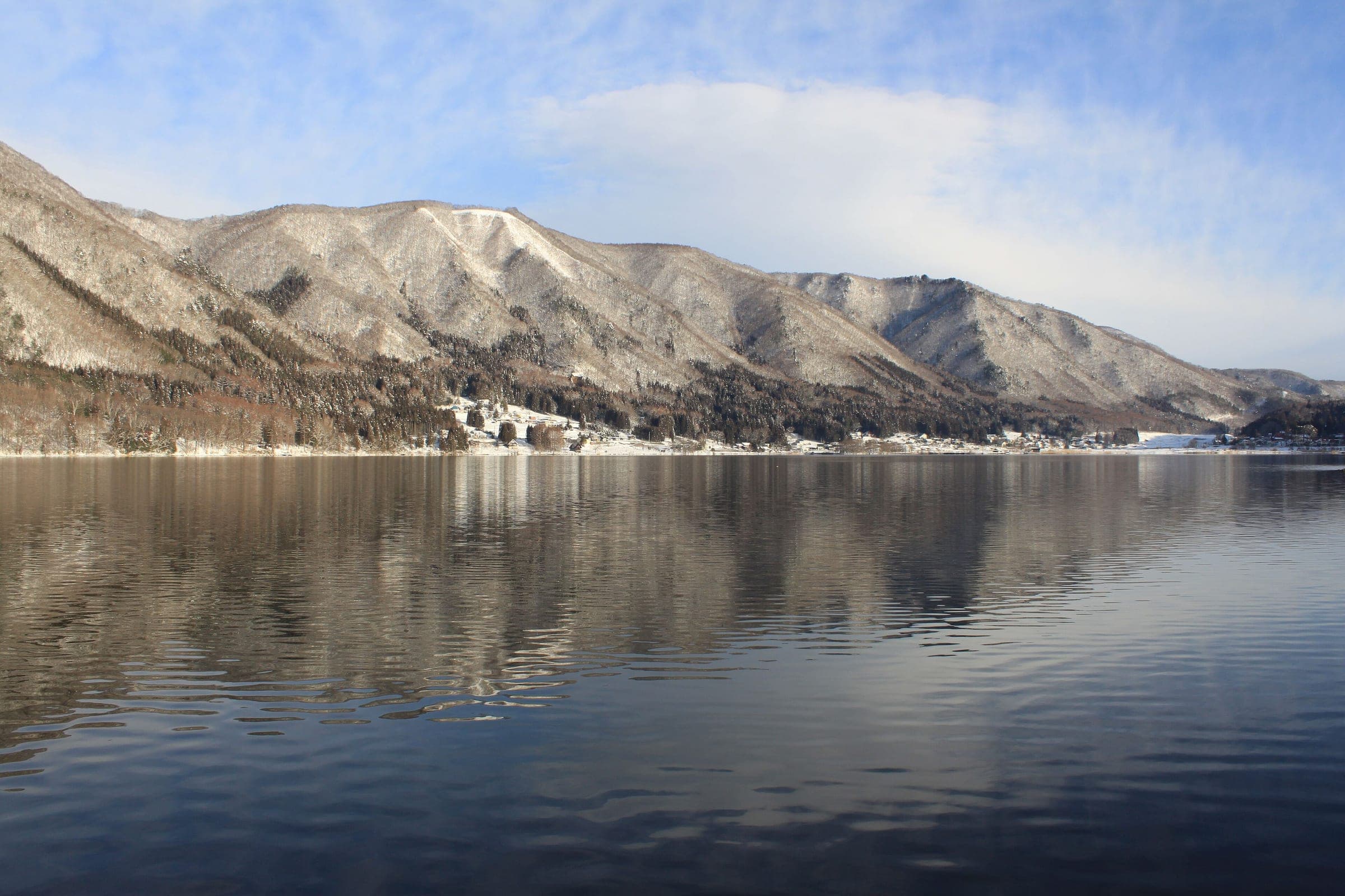 A snow-dusted ridge reflects in the calm water of Lake Kizaki in Omachi.