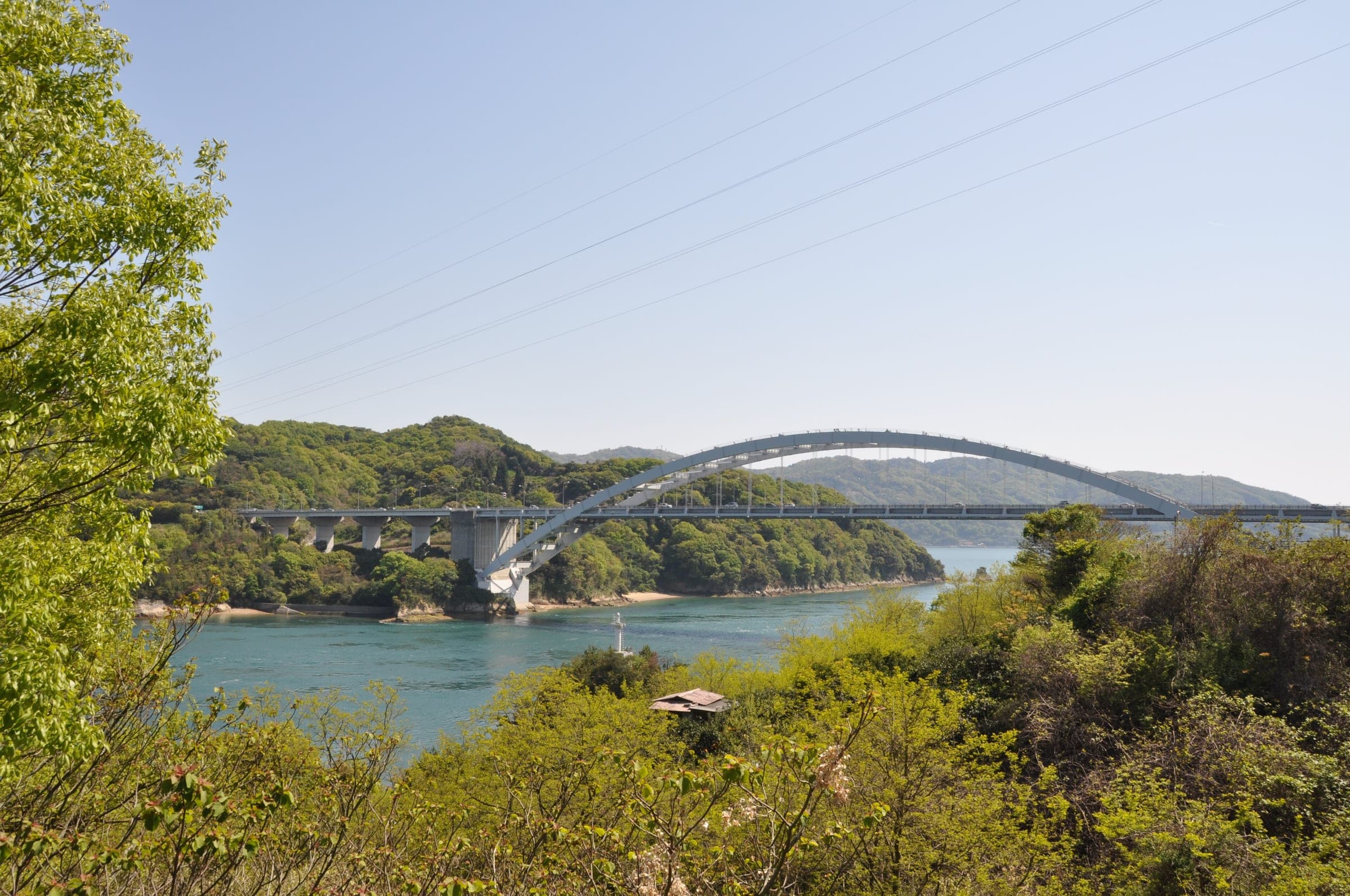 The steel arch of the Omishima Bridge spans a narrow green channel between Omishima and Hakatajima.