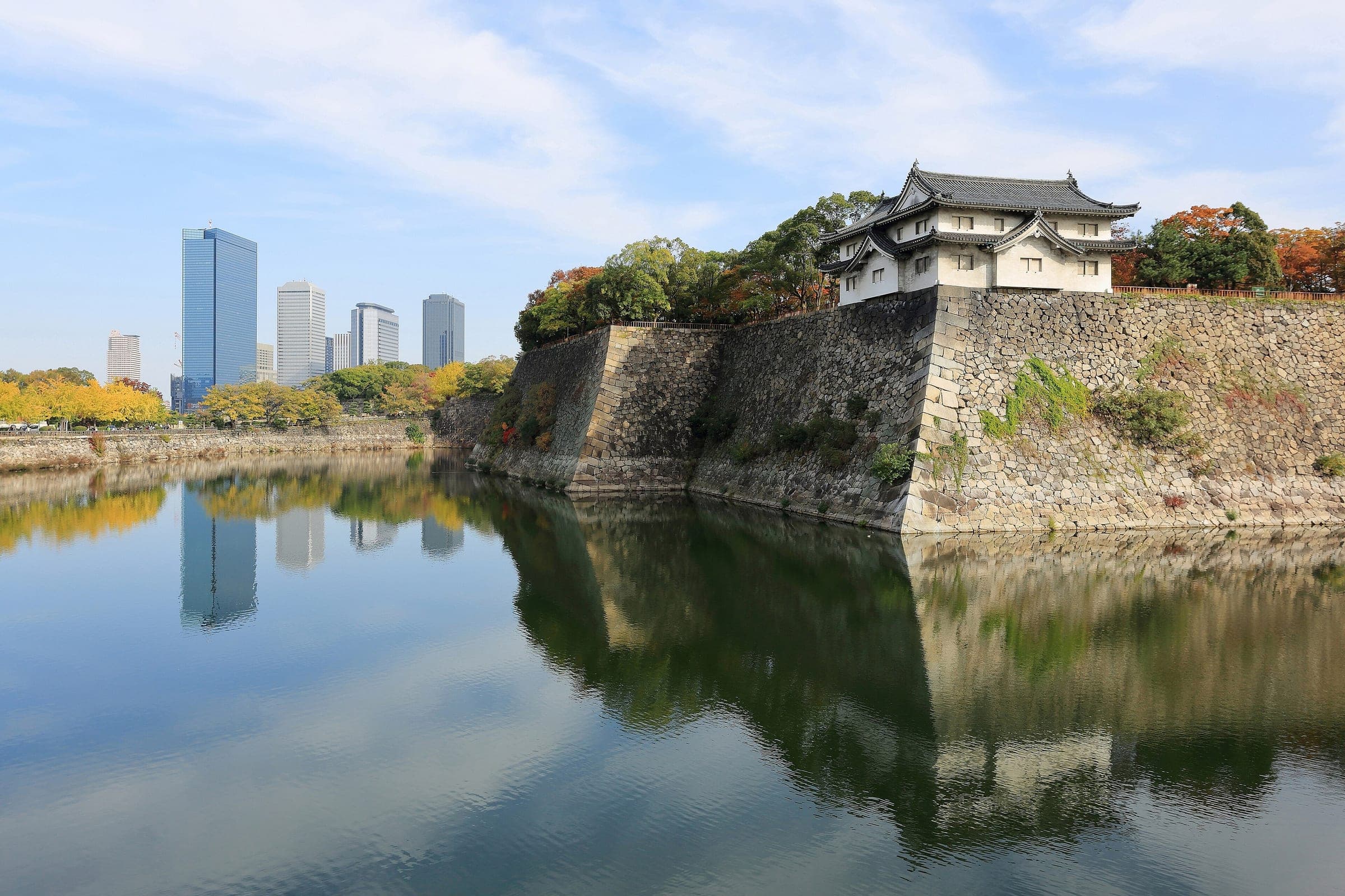 The stone walls of Osaka Castle reflect in the outer moat beside the towers of Osaka Business Park
