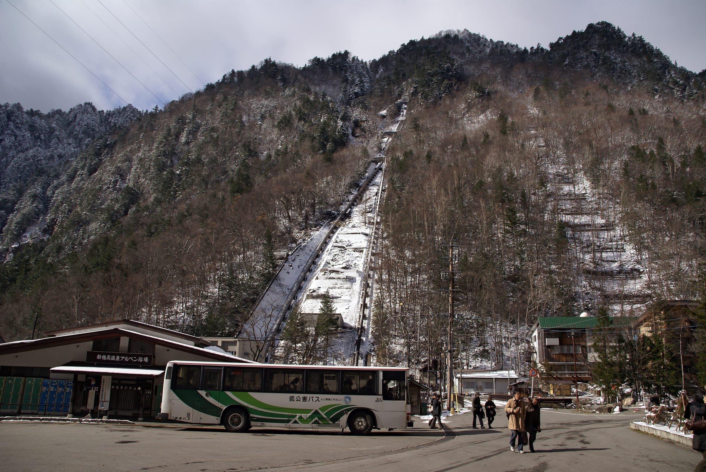 A Nohi bus waits at the Shin-Hotaka Onsen terminal below a steep slope dusted with snow