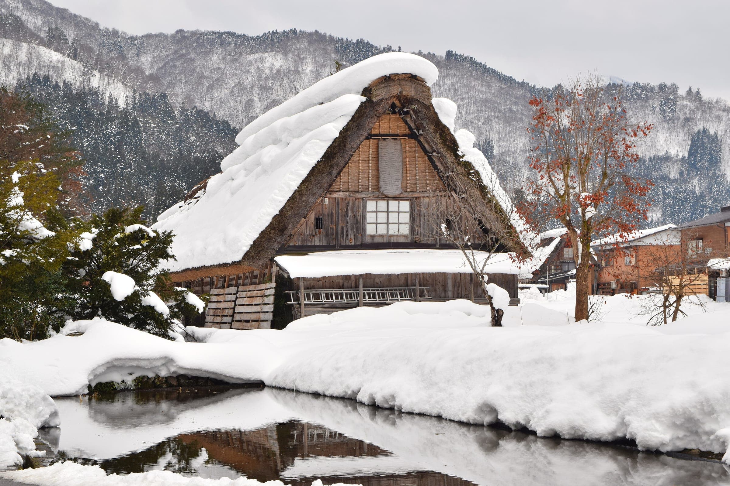 A gassho-zukuri farmhouse under deep snow reflects in a pond in Shirakawa-go