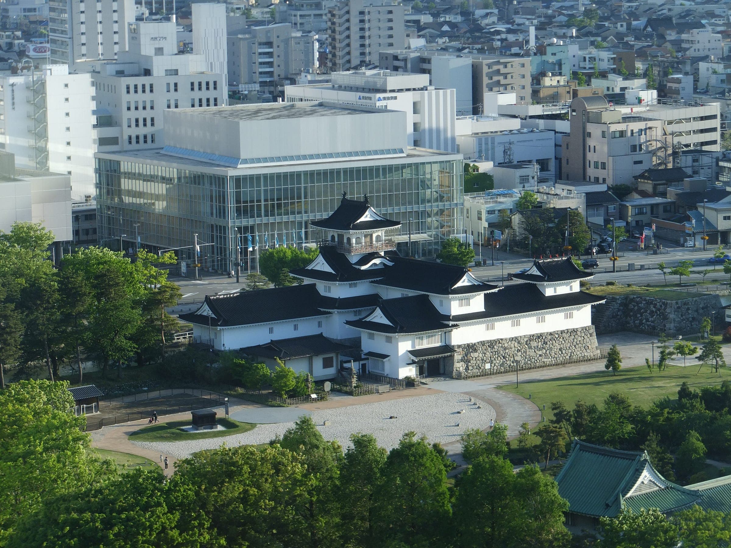 Toyama Castle's white walls and turrets sit in a green park among city buildings in central Toyama
