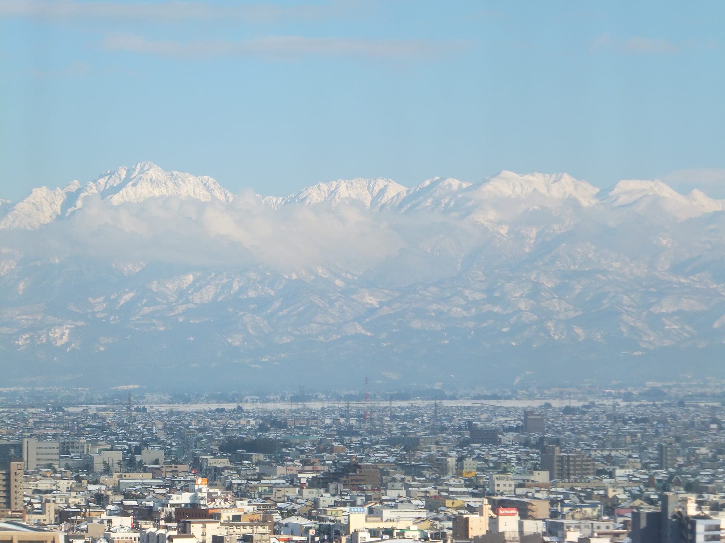 The snow-covered Tateyama range towers over the rooftops of Toyama city on a clear winter day