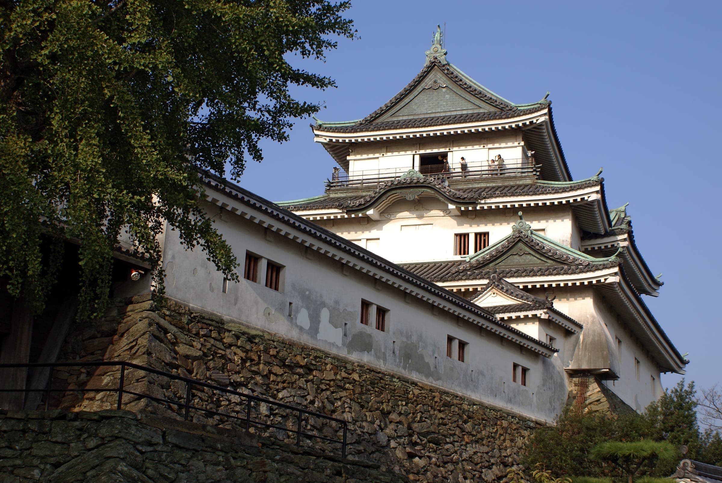 Wakayama Castle's white keep rises over its stone walls against a deep blue sky
