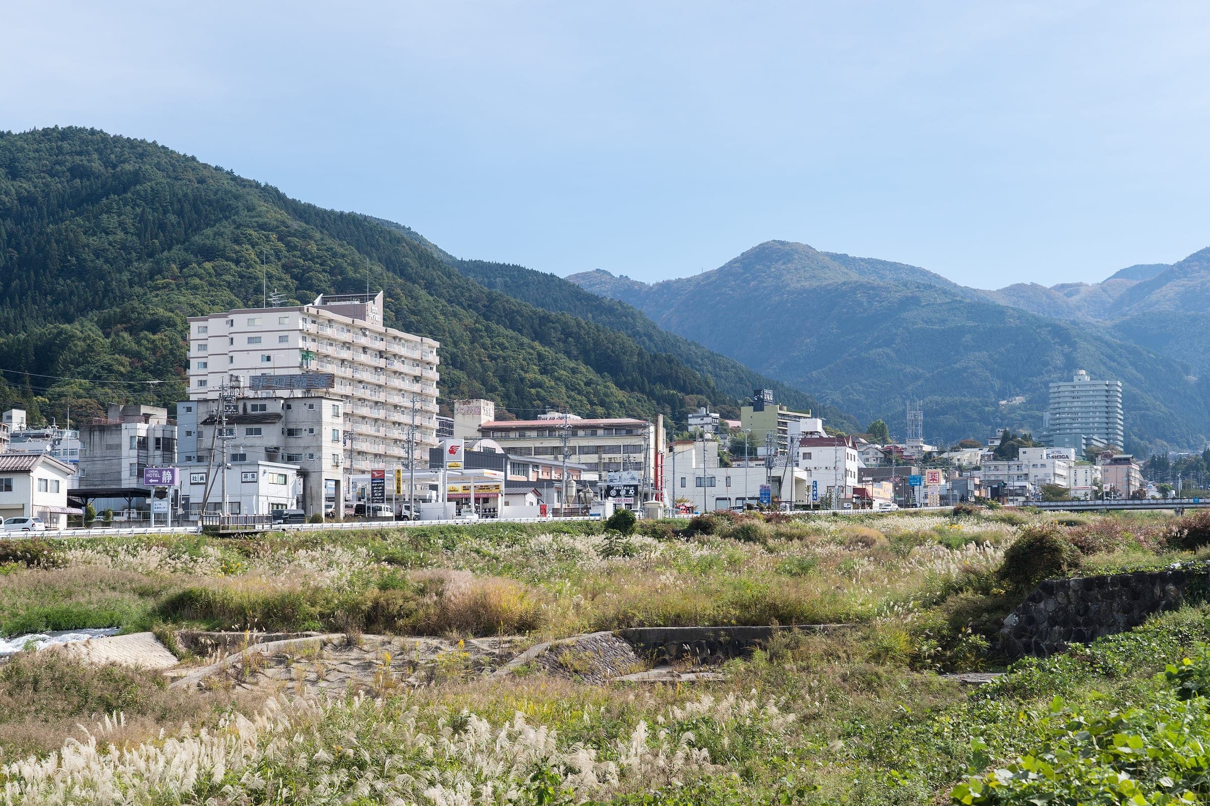 Hotels of Yamanouchi rise above the grassy Yomase riverbank under wooded mountains in October.