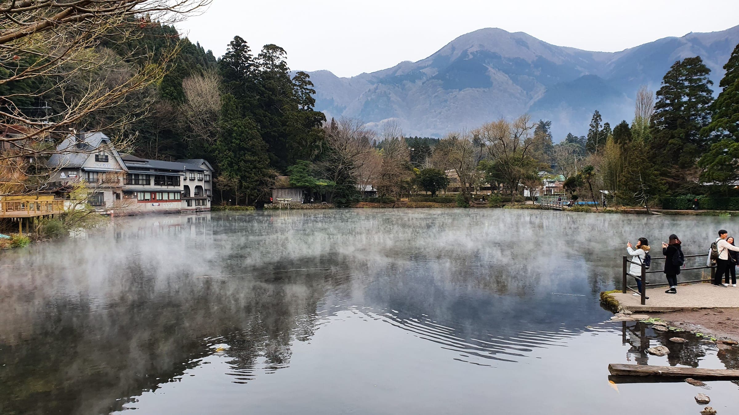 Mist lifts off Lake Kinrin on a January morning while visitors watch from the shore in Yufuin.